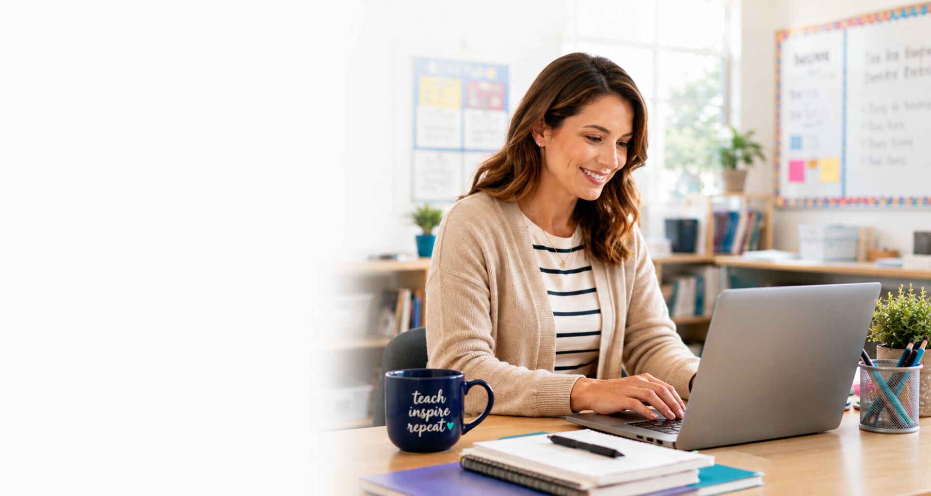 A teacher planning lessons at her laptop in a bright, welcoming classroom